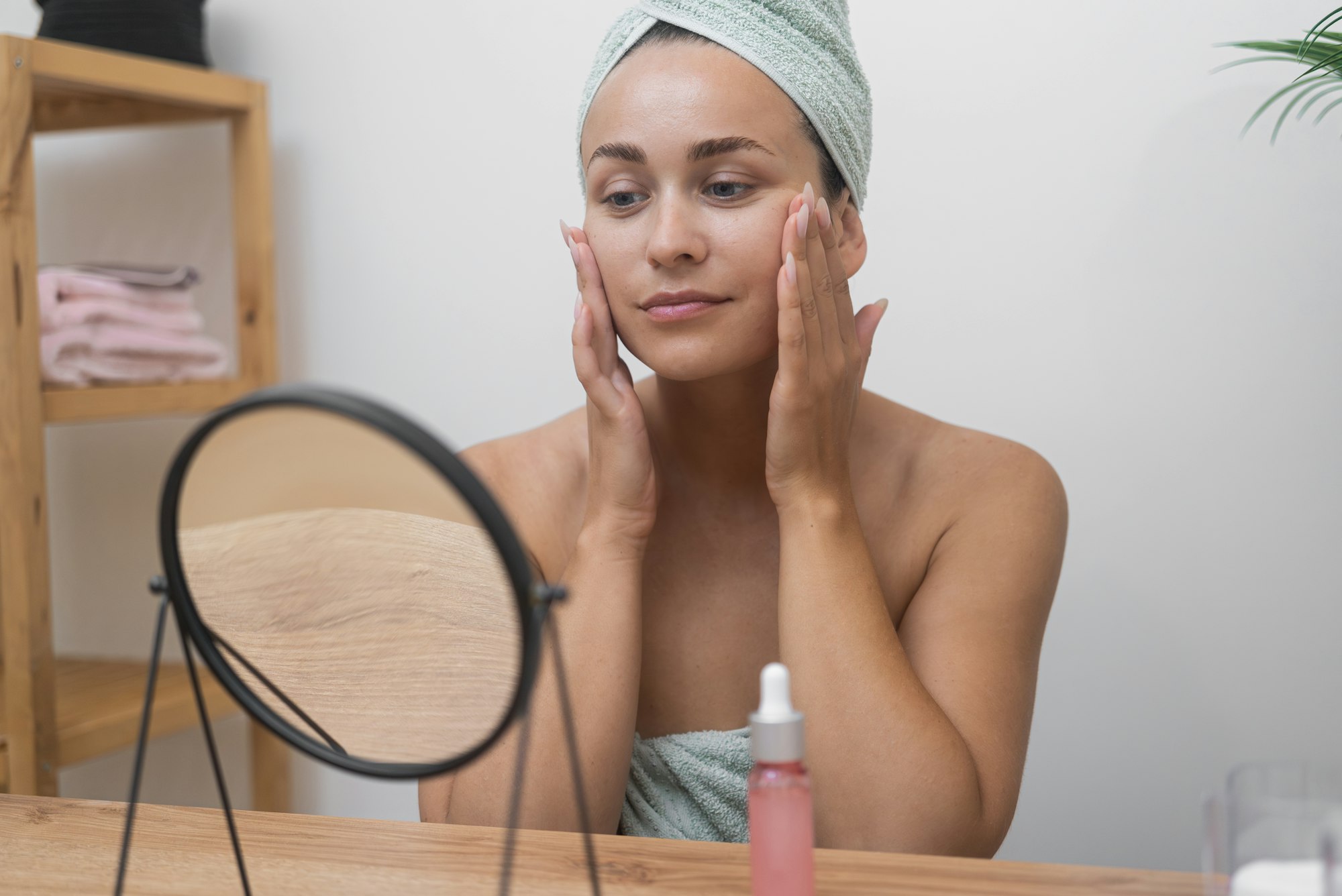 lady, towel-clad, enjoys skincare spa day, admiring her smooth skin in the table mirror.